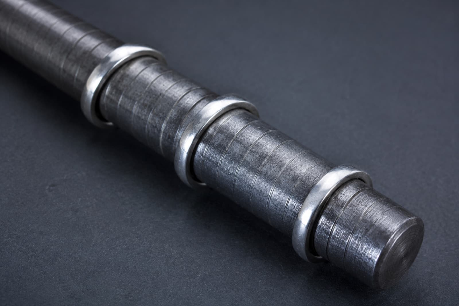 A steel ring sizing mandrel lying at an angle with three plain silver bands slid onto it at different heights