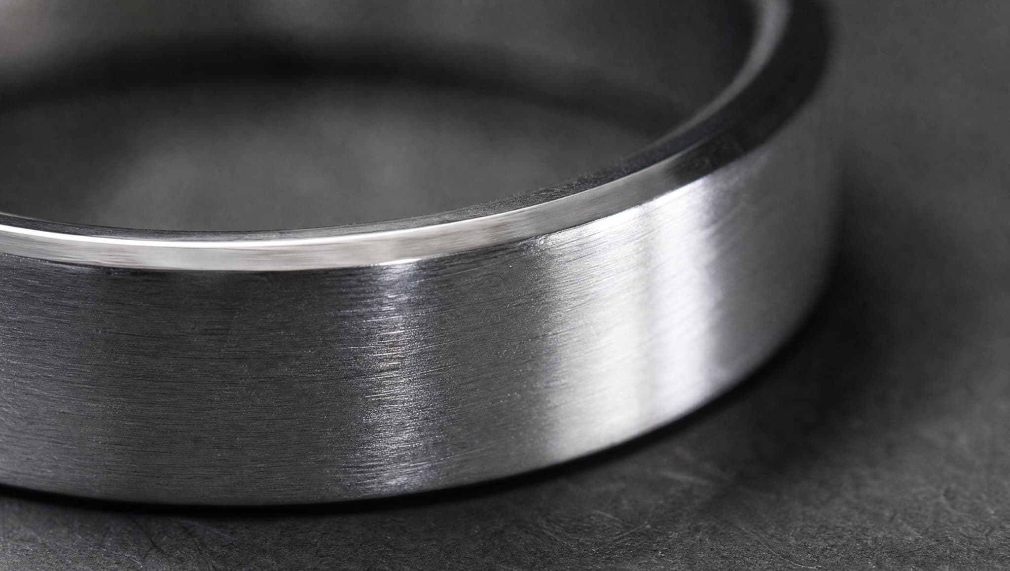 Extreme close-up of a plain sterling silver band, showing the brushed grain of the outer face and the polished chamfer at its edge