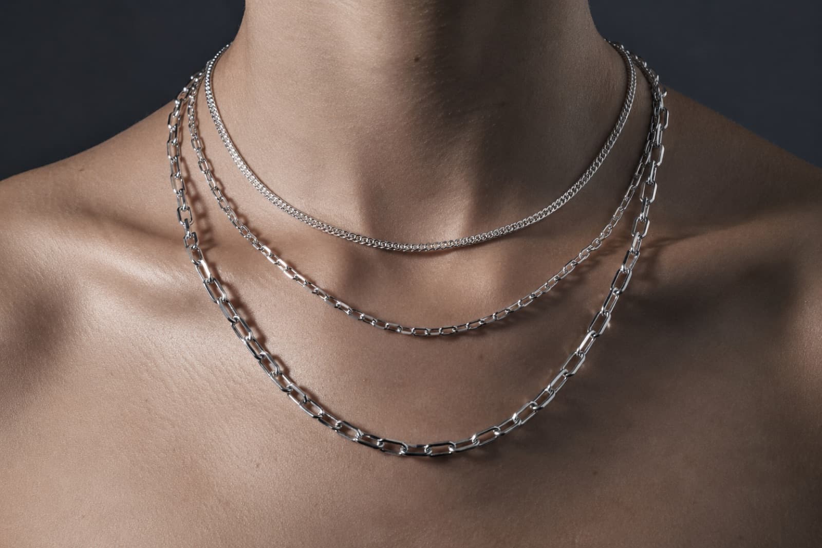 Three plain silver chains of different lengths and gauges layered at the collarbone
